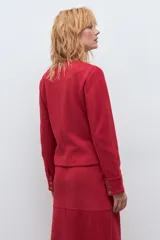Chaqueta de textura simil gamuza en color rojo, con cuello redondo, cierre frontal mediante botones metálicos y bolsillos laterales.