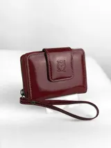 Mini billetera de cuero charolado color rojo, con cierre perimetral y solapa frontal con broche, decorada con un logo de búho grabado.