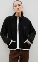 Campera de sherpa negra con cierre frontal, cuello alto y detalles de ribete en color blanco. Presenta un bordado azul en el pecho con el logo de la marca.