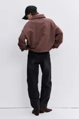 Sudadera de algodón color marrón, con cuello polo y cierre frontal de botones. Presenta un diseño holgado, mangas largas con puños elásticos y un pequeño parche bordado en forma de corazón en el pecho.