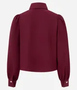 Camisa de crepé color blanco, con cuello inglés, manga larga abullonada con puños abotonados y cierre frontal oculto con botón diferenciado en el cuello.