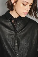 Camisa de cuero ovino color verde oliva, con cuello clásico, cierre frontal con botones y mangas largas con puños abotonados. Presenta un corte holgado y diseño tipo sobrecamisa.