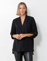 Blusa de tejido piqué color fucsia, con escote en V y pliegue central delantero. Presenta mangas largas con sistema de ajuste mediante presilla y botón, y tajos laterales en el ruedo.