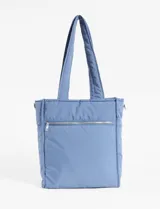 Cartera shopper azul acolchada con pespuntes ondulados. Tiene doble asa de hombro y correa extraíble regulable. Incluye cierre principal, bolsillo interior y bolsillo trasero con cierre.