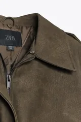 Cazadora color verde militar con efecto ante, cuello solapa con aplicación de pelo sintético desmontable, manga larga con puño, trabillas en los hombros y bolsillos frontales con solapa y botón. Cierre frontal con cremallera y botones ocultos.