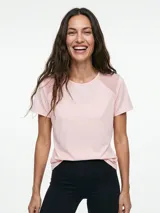 Remera deportiva de manga corta color rosado, con inserciones de tela de malla en los hombros y escote redondo.