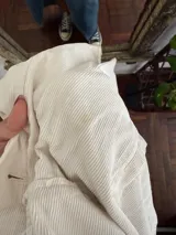 Campera de pana color blanco marfil, con bolsillos frontales con solapa, bolsillos laterales ojetes, cierre con botones oscuros y detalles de terminaciones deshilachadas.