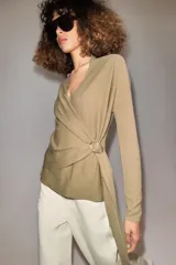 Chaqueta de punto de color tostado, con escote en V y manga larga. Diseño cruzado al frente con cinturón lazada en el mismo tejido y detalle de hebilla metálica circular en el lateral.