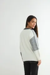 Buzo de tejido de punto con diseño de bloques de color en tonos blanco y gris, de cuello redondo y manga larga.