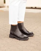 Botinetas tipo Chelsea de cuero negro, con paneles laterales elásticos y suela track dentada de goma. Presentan una combinación de texturas entre cuero mate y cuero charolado en la puntera y el talón.
