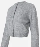 Cardigan cropped de punto color gris, con cuello redondo, manga larga, cierre frontal con botones y dos bolsillos delanteros. Presenta terminaciones acanaladas en puños y bajo.