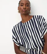 Blusa de viscosa con estampado de rayas verticales blancas y azul marino. Tiene cuello redondo, mangas cortas con detalle de lazo ajustable en los laterales y cierre de botón en la espalda.