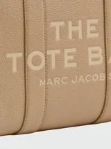 Cartera tipo tote de Marc Jacobs, confeccionada en cuero granulado color azul marino. Presenta el logo de la marca estampado en el frente, doble asa superior y correa ajustable y extraíble para llevar al hombro o cruzada.