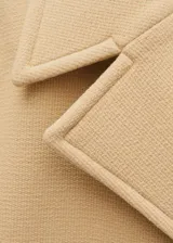 Abrigo de lana virgen en color beige, con diseño de doble botonadura, cuello con solapas de muesca y bolsillos laterales. Presenta un corte recto y mangas largas.