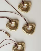 Collar con dije de forma irregular y orgánica en tono dorado, suspendido de un cordón de algodón marrón.