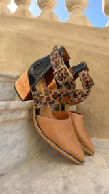 Zapatos de cuero color tostado con puntera fina y taco bloque de madera de 6 cm. Cuentan con tiras cruzadas con estampado animal print de leopardo en el empeine, talón negro y tira al tobillo con hebilla metálica ajustable.
