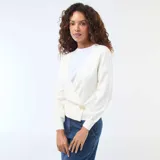 Sweater de punto color blanco con diseño cruzado tipo cárdigan, escote en V profundo y cierre lateral con un botón dorado. Presenta mangas largas con puños ajustados y un corte entallado a la cintura.
