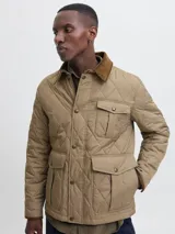 Campera acolchada de diseño matelasse en color tostado, con cuello camisero en pana marrón, cierre frontal con broches a presión, bolsillos frontales con solapa y puños ajustables.