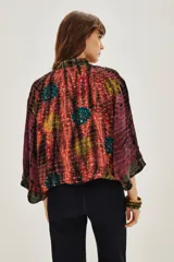 Kimono de estilo abierto con mangas anchas, confeccionado en viscosa con un diseño estampado que combina patrones tipo tie-dye y patchwork en tonos vibrantes. Presenta detalles de aplicaciones decorativas y forro interior.