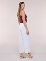 Pantalón negro de calce relajado y caída fluida, confeccionado en poliéster con textura de crepé. Tiene cintura alta elastizada estilo pull on con un aplique de cadena metálica decorativa, y pierna de corte ancho tipo wide leg corto por arriba del tobillo.