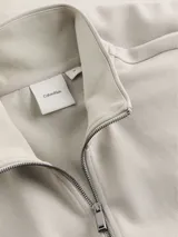 Buzo de cuello alto con cierre frontal completo, confeccionado en una mezcla de algodón y poliéster. Presenta un diseño minimalista con logo de Calvin Klein en el pecho, puños y bajo acanalados, y bolsillos laterales.