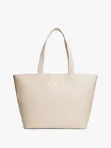Cartera tipo tote color beige con acabado liso, doble asa superior de cinta y logotipo metálico dorado de la marca en la parte frontal. Cuenta con compartimiento principal con cierre de cremallera.