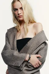 Pulsera rígida de metal plateado con diseño articulado y terminaciones con piedras incrustadas en tono marrón.