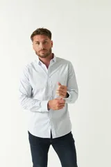 Camisa de manga larga para hombre, color blanco con finas rayas verticales celestes. Presenta un corte slim, cuello camisero y logo bordado en el pecho.