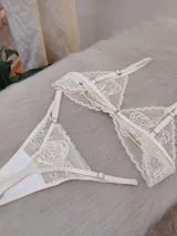 Conjunto de lencería compuesto por un bralette triangular de encaje floral y una bombacha tipo tanga a juego con detalles de encaje y tiras ajustables.