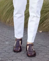 Sandalias estilo romano de cuero marrón oscuro, con diseño de tiras entrelazadas, talón cerrado y hebilla metálica de ajuste lateral.