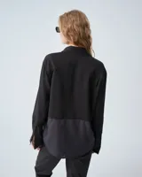 Camisa negra combinada bicolor confeccionada en telas italianas, de silueta holgada. Tiene cuello camisero, cartera con botones, y un bolsillo plaqué. Las mangas largas presentan pliegues en los puños y tablitas en la espalda.