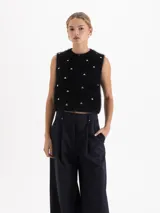 Top sin mangas de cuello redondo y corte cropped, confeccionado en tejido de angora y lana con textura suave. Presenta apliques metálicos en forma de corazón distribuidos por toda la prenda.