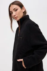 Buzo de sherpa con textura capitoneada, color bordó, con cuello alto y cierre frontal parcial. Presenta bolsillos laterales y calce relajado.