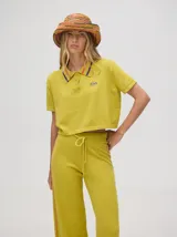 Chomba crop color beige, confeccionada en algodón, con cuello camisero que presenta rayas marrones y granates. Posee un pequeño logo bordado en el pecho.