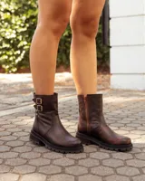 Botas de caña media color marrón con acabado desgastado, confeccionadas en cuero. Presentan una suela chunky dentada, cierre lateral y dos correas decorativas con hebillas metálicas en el lateral exterior.