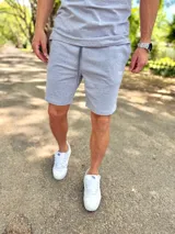 Conjunto deportivo gris melange compuesto por remera de manga corta y short con cordón ajustable en la cintura.