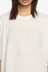 Camiseta blanca de algodón orgánico, corte oversize, con escote redondo y mangas cortas anchas. Presenta un logo grande en relieve en el frente.