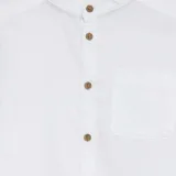 Camisa blanca de lino, de manga larga con cuello mao y abotonadura frontal con botones marrones.