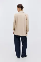 Blazer de sarga color beige, con solapas de pico, frente abierto y bolsillos delanteros ribeteados con solapa.