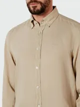 Camisa de vestir color beige claro, de corte clásico, con cuello abotonado y mangas largas.