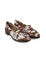 Mocasín de cuero estilo animal print con estampado de vaca en tonos marrón y blanco, con detalle de antifaz en el empeine y suela plana con pequeño tacón.
