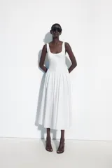 Vestido midi de corte corsetero color blanco, con escote redondo, tirantes finos y detalle de lazo en el delantero. Falda con frunces y cierre en la espalda con cremallera oculta.
