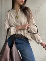 Camisa beige de manga larga con detalles de vainica vertical en el frente y cierre frontal de botones.