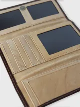 Billetera de cuero combinada en tonos camel y marrón, de formato rectangular con solapa. Cuenta con un parche central decorativo con logo grabado y detalles de costura perimetral.