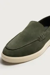 Mocasines casuales para hombre confeccionados en piel con acabado serraje de color verde oscuro, con detalle de bordón pespunteado, horma redonda y suela de goma en contraste de color beige claro.