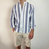 Camisa de manga larga con cuello mao, confeccionada en tejido de lino a rayas verticales en tonos blanco y celeste. Presenta cierre frontal con botones y corte clásico.