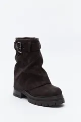Bota de caña media color negro, con suela robusta dentada y detalle de hebilla ajustable en la parte superior. Presenta una argolla metálica lateral y un diseño de estética urbana con acabado texturizado.
