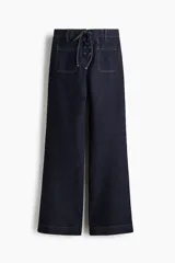 Jean de tiro alto en denim azul oscuro, con corte acampanado desde la rodilla. Presenta un diseño con cordones frontales para ajuste en la cintura, bolsillos delanteros y traseros, y costuras a contratono.