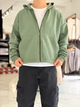 Campera tipo canguro con cierre frontal completa y capucha, de corte boxy fit en color blanco marfil. Presenta bolsillos frontales tipo parche y puños y dobladillo en rib elástico.