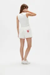 Short ancho de tiro alto confeccionado en mezcla de lino y viscosa, de color blanco. Presenta detalles bordados de un corazón y frutillas en la parte frontal, además de una línea ondulada decorativa en contraste en el ruedo. Cuenta con cintura elástica.